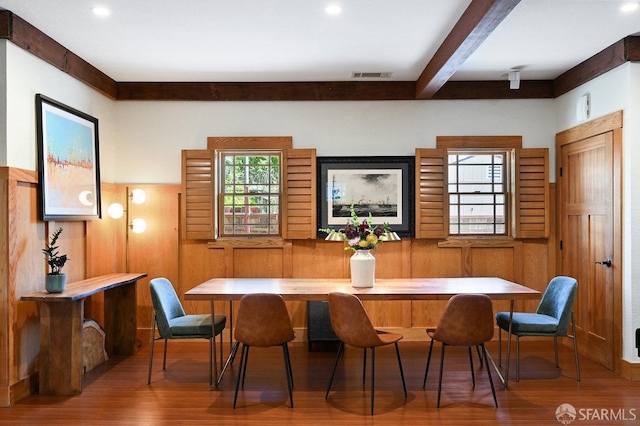dining space featuring beamed ceiling, wood walls, wood finished floors, and visible vents