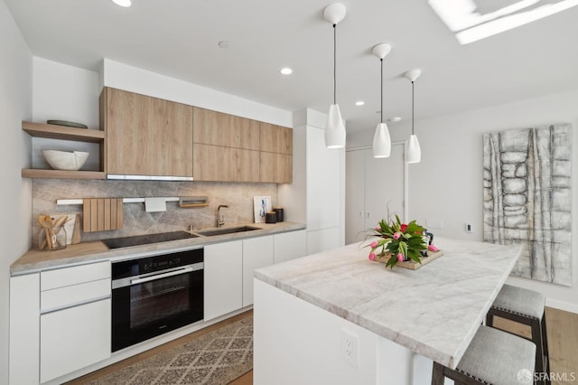 kitchen featuring white cabinets, sink, decorative light fixtures, and stainless steel oven