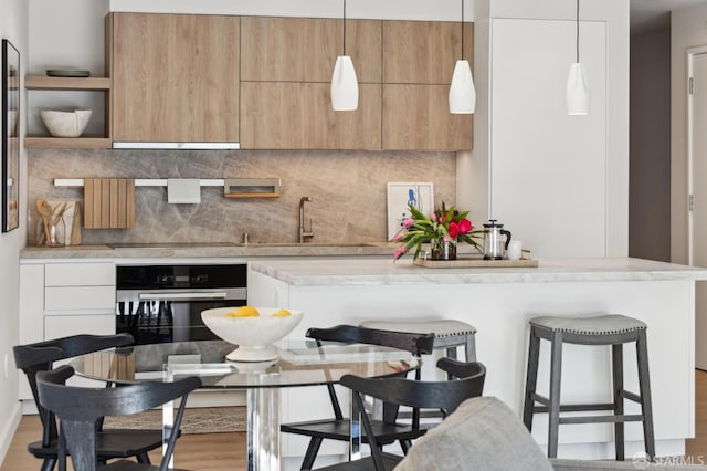 kitchen with decorative light fixtures, stainless steel oven, decorative backsplash, and white cabinetry