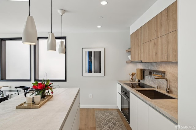 kitchen with white cabinets, sink, hanging light fixtures, light wood-type flooring, and black oven