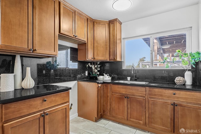 kitchen with light tile patterned floors, dark stone countertops, sink, and backsplash