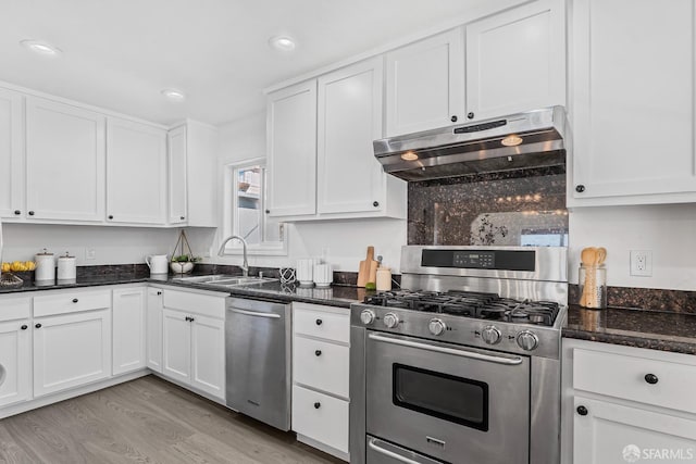 kitchen featuring sink, white cabinetry, stainless steel appliances, light hardwood / wood-style floors, and dark stone counters