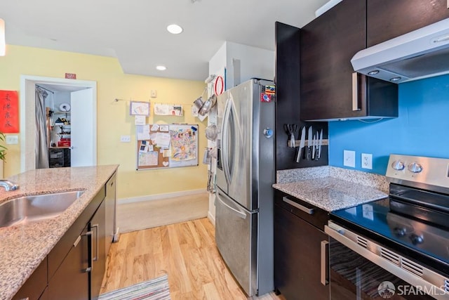 kitchen with light wood-style floors, light stone countertops, stainless steel appliances, under cabinet range hood, and a sink