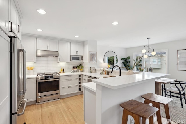 kitchen featuring a breakfast bar, white cabinetry, hanging light fixtures, light hardwood / wood-style flooring, and appliances with stainless steel finishes