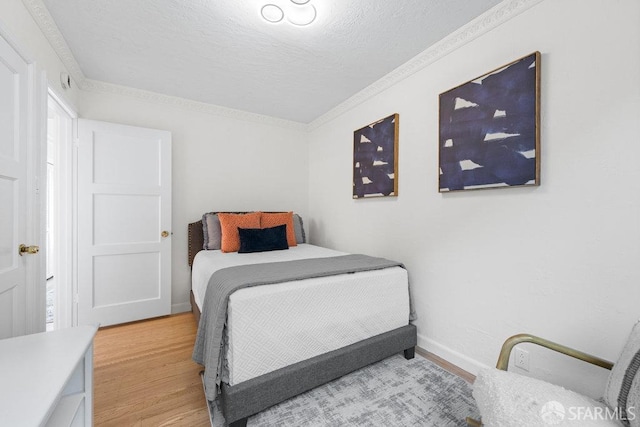 bedroom featuring a textured ceiling, baseboards, light wood-style flooring, and crown molding