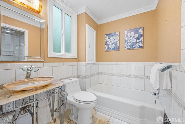 bathroom featuring toilet, a sink, tile walls, a bath, and crown molding