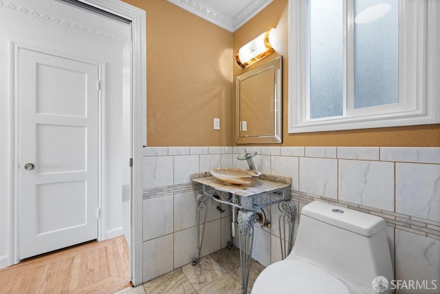 bathroom featuring marble finish floor, a wainscoted wall, tile walls, toilet, and a sink