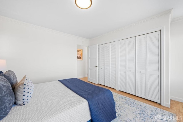 bedroom featuring baseboards, ornamental molding, wood finished floors, and multiple closets