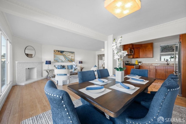 dining room featuring a brick fireplace, light wood-style flooring, and crown molding