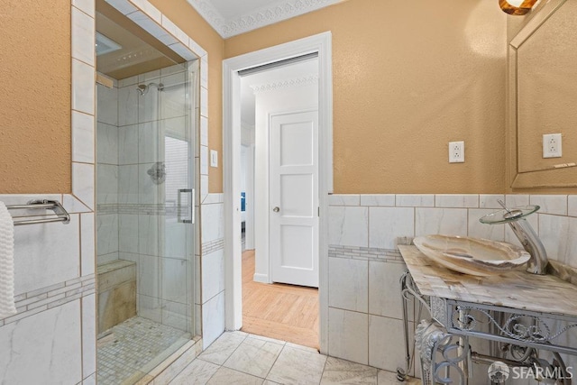 full bath with a wainscoted wall, a textured wall, a shower stall, and tile walls