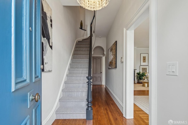 foyer entrance featuring stairway, baseboards, wood finished floors, and a chandelier