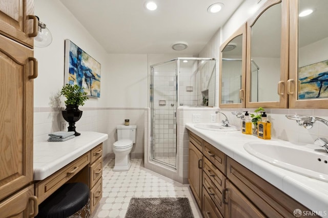 full bath with a sink, tile walls, a stall shower, and toilet