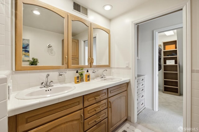 bathroom featuring double vanity, a walk in closet, visible vents, and a sink