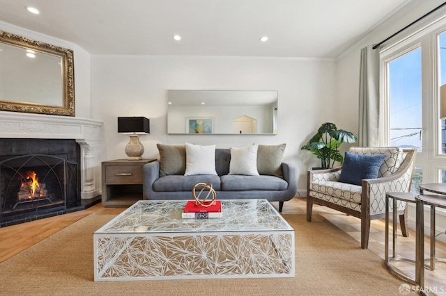 living room with recessed lighting, a lit fireplace, ornamental molding, and wood finished floors
