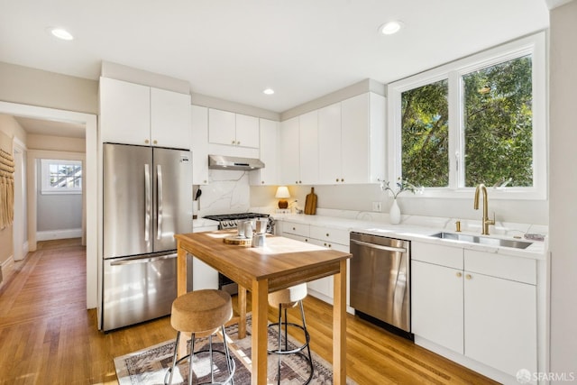 kitchen with stainless steel appliances, white cabinetry, sink, and light hardwood / wood-style floors