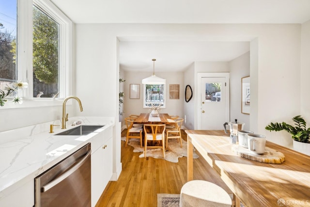 kitchen featuring sink, white cabinetry, hanging light fixtures, light hardwood / wood-style floors, and stainless steel dishwasher