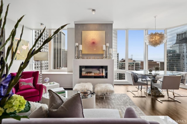 living area with a view of city, expansive windows, a glass covered fireplace, and wood finished floors