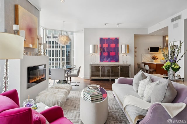 living room featuring a glass covered fireplace, baseboards, visible vents, and wood finished floors