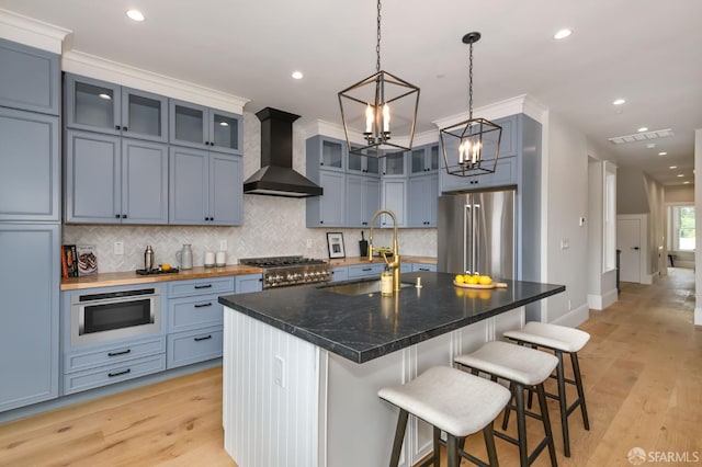 kitchen featuring wood counters, wall chimney exhaust hood, a kitchen bar, high end fridge, and a kitchen island with sink