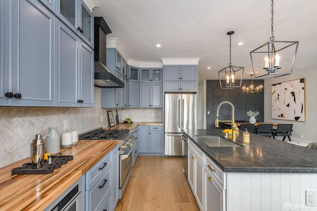 kitchen featuring sink, high end appliances, pendant lighting, a kitchen island with sink, and wall chimney range hood