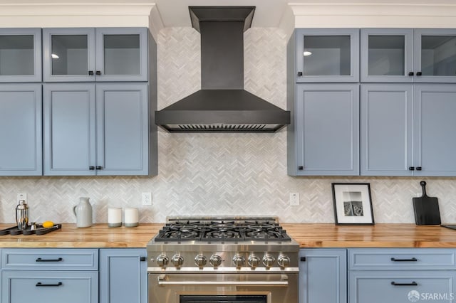 kitchen featuring butcher block countertops, backsplash, high end range, blue cabinetry, and wall chimney range hood