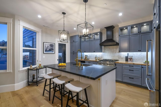 kitchen featuring wall chimney exhaust hood, sink, decorative light fixtures, stainless steel appliances, and a kitchen island with sink