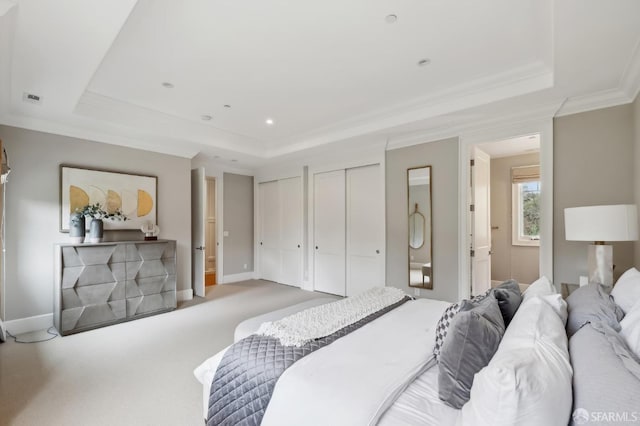 bedroom with ornamental molding, a tray ceiling, light colored carpet, and ensuite bathroom