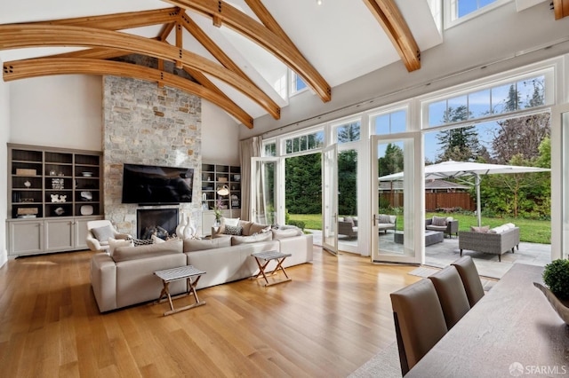 living room with high vaulted ceiling, a stone fireplace, built in features, light wood-type flooring, and beamed ceiling