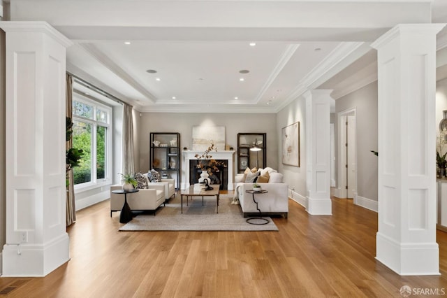 living room featuring crown molding, a raised ceiling, light hardwood / wood-style flooring, and decorative columns