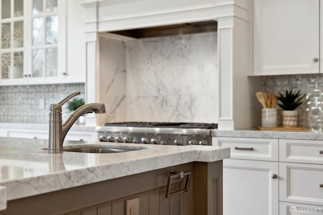 kitchen featuring backsplash, white cabinetry, sink, and light stone countertops