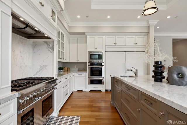 kitchen featuring built in appliances, white cabinetry, light stone countertops, and decorative light fixtures