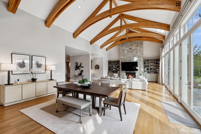 dining space featuring a stone fireplace, high vaulted ceiling, and light hardwood / wood-style flooring