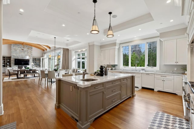 kitchen with light stone counters, a raised ceiling, a kitchen island, decorative light fixtures, and white cabinetry