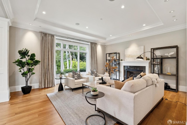 living room featuring a raised ceiling, ornamental molding, a high end fireplace, and light hardwood / wood-style flooring