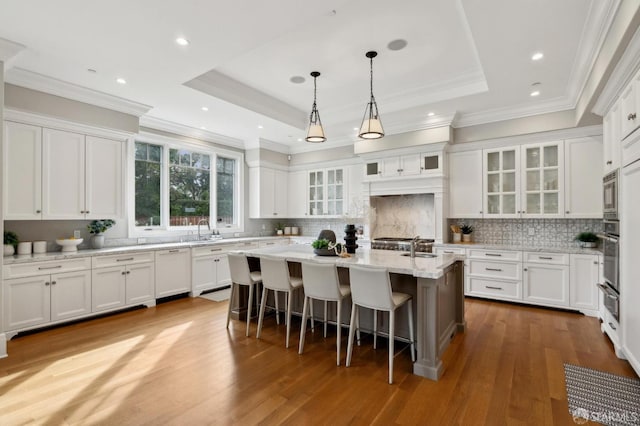 kitchen featuring appliances with stainless steel finishes, a tray ceiling, white cabinets, light hardwood / wood-style floors, and an island with sink