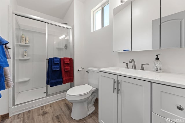 bathroom featuring toilet, a stall shower, wood finished floors, and vanity