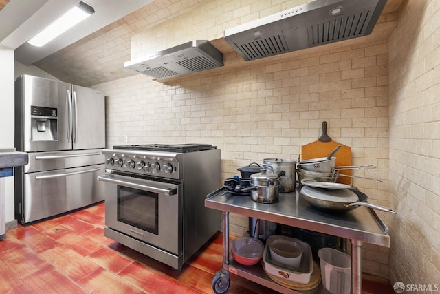 kitchen featuring lofted ceiling, wall chimney exhaust hood, brick wall, and stainless steel appliances