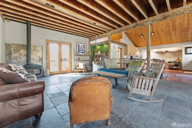 interior space featuring a wood stove, stone tile floors, vaulted ceiling, and french doors