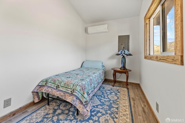 bedroom with a wall unit AC, wood finished floors, electric panel, and baseboards