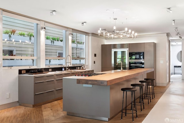 kitchen featuring gray cabinets, butcher block counters, built in appliances, and a breakfast bar area