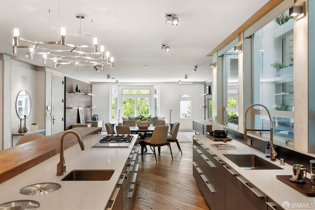 kitchen featuring stainless steel gas stovetop, sink, dark wood-type flooring, and decorative light fixtures