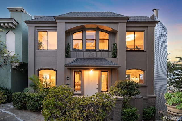 view of front of home with a shingled roof, a balcony, and stucco siding