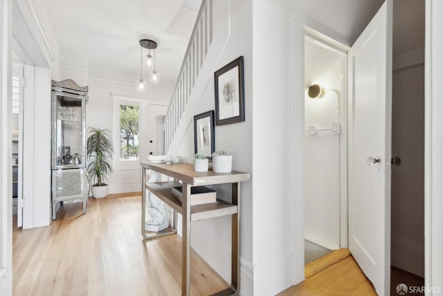 hall with stairs, crown molding, and light wood-style floors