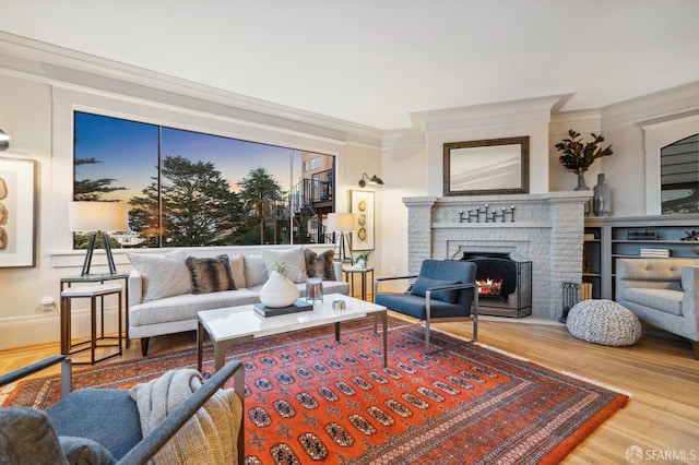 living room with a brick fireplace, ornamental molding, and wood finished floors