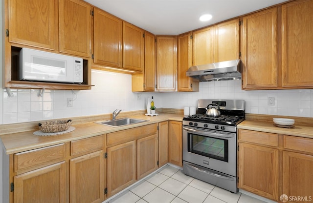 kitchen with white microwave, under cabinet range hood, a sink, light countertops, and gas stove