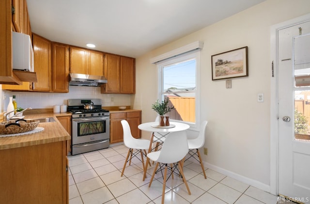 kitchen featuring stainless steel range with gas cooktop, decorative backsplash, a healthy amount of sunlight, a sink, and under cabinet range hood