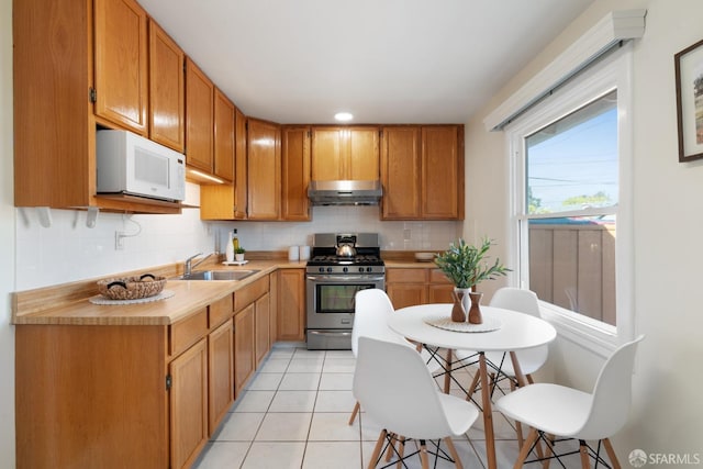 kitchen with gas range, white microwave, light countertops, under cabinet range hood, and a sink