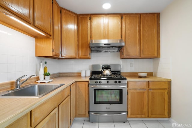 kitchen with tasteful backsplash, light countertops, a sink, stainless steel gas range, and under cabinet range hood