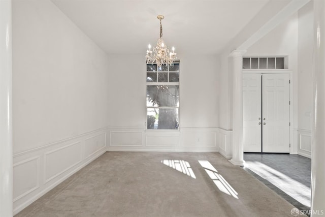 carpeted spare room with decorative columns and a notable chandelier