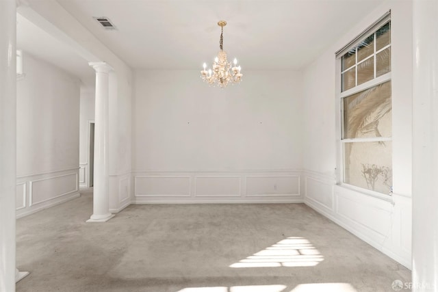 empty room with decorative columns, light carpet, and a notable chandelier